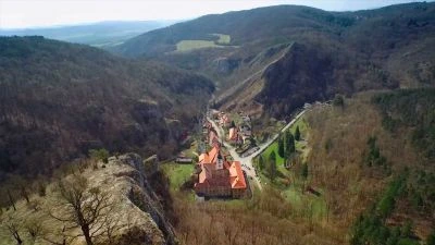 Pohled na údolí s vesnicí obklopenou lesnatými pahorky.