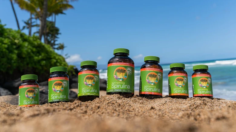 Fľaše spiruliny na pláži s mořem v pozadí.