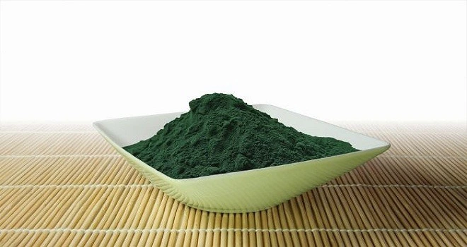 Hromada tmavě zelené prášku z řasy Spirulina v bílé míse.